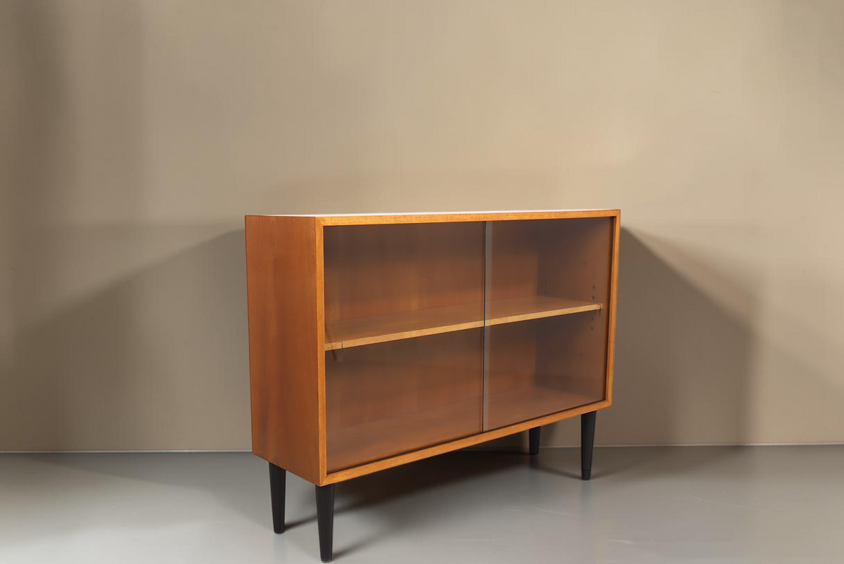 Vintage Space Mid Century Vitrine mit Glasschiebetüren, Holzkorpus und schwarzen konischen Füßen vor weißem Hintergrund