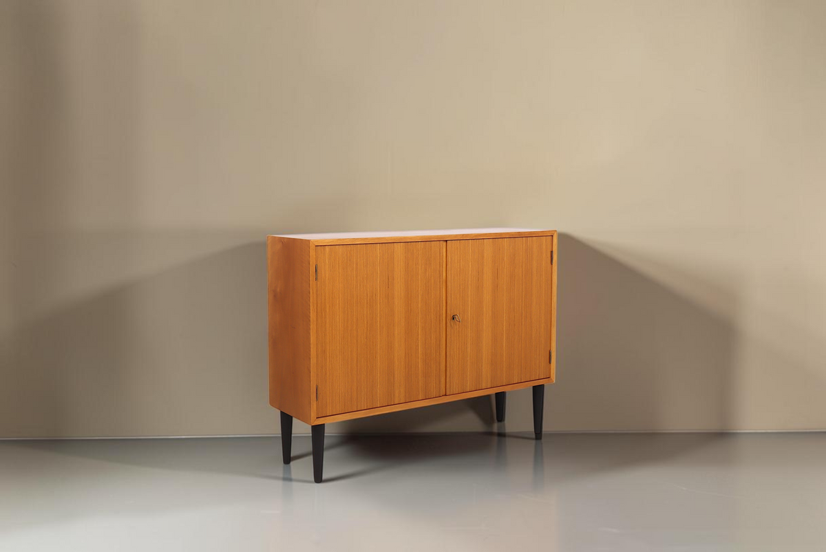 Vintage Space Mid Century Kommode aus Holz mit zwei Türen und schwarzen konischen Füßen vor weißem Hintergrund
