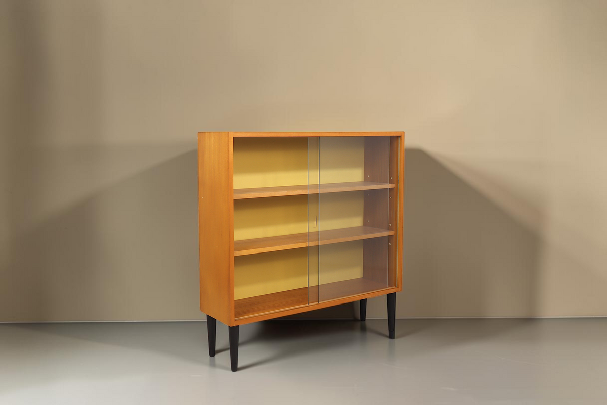 Vintage Space Hellerau Mid-Century Vitrine mit Holzfurnier, Glasschiebetüren und gelber Rückwand auf schwarzen Beinen