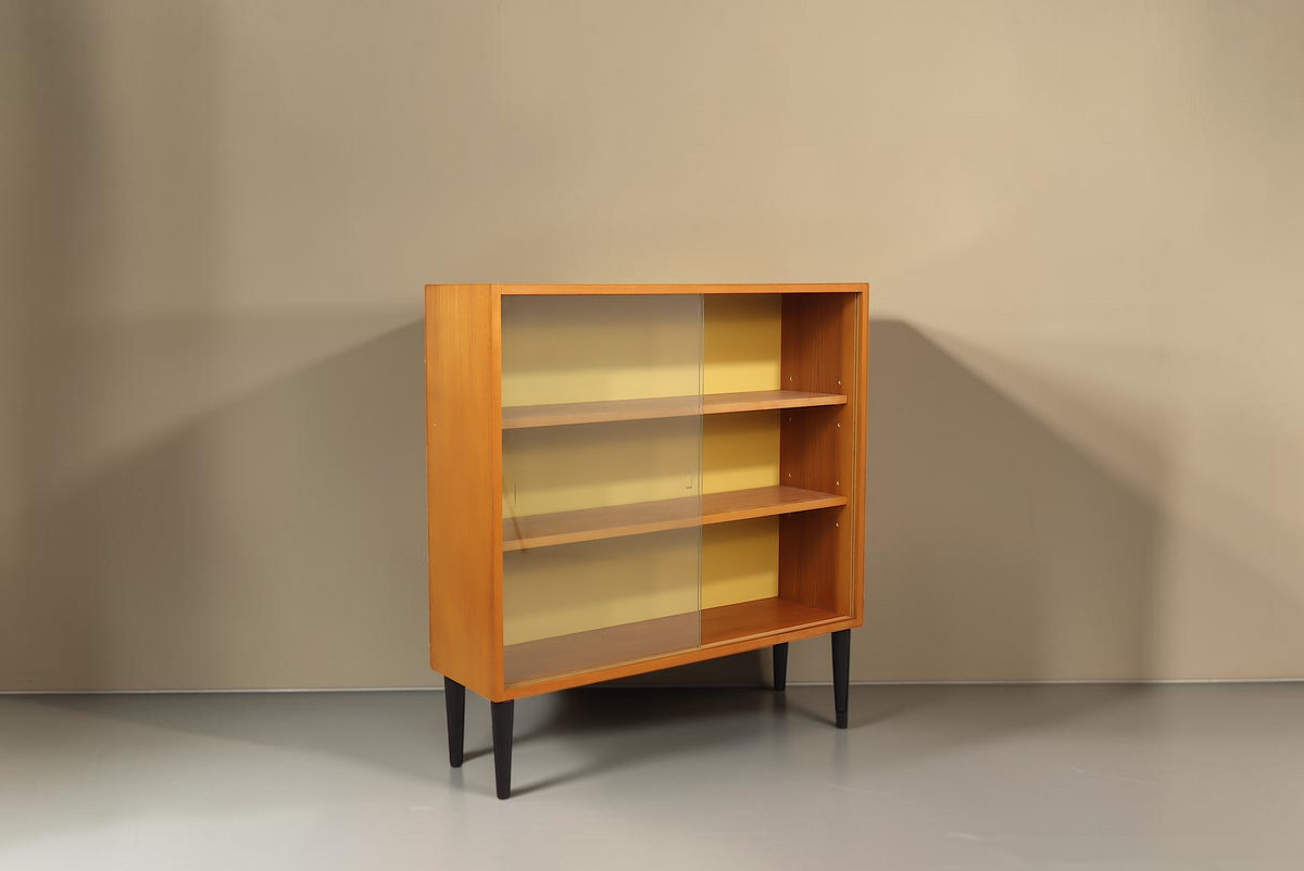 Vintage Space Hellerau Mid Century Vitrine mit Glasschiebetüren, Holzfurnier und gelber Rückwand auf schwarzen Beinen