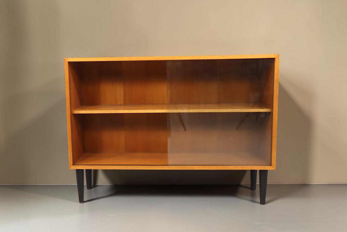 Vintage Space Mid Century Vitrine aus Holz mit Glasschiebetüren und schwarzen konischen Füßen vor weißem Hintergrund