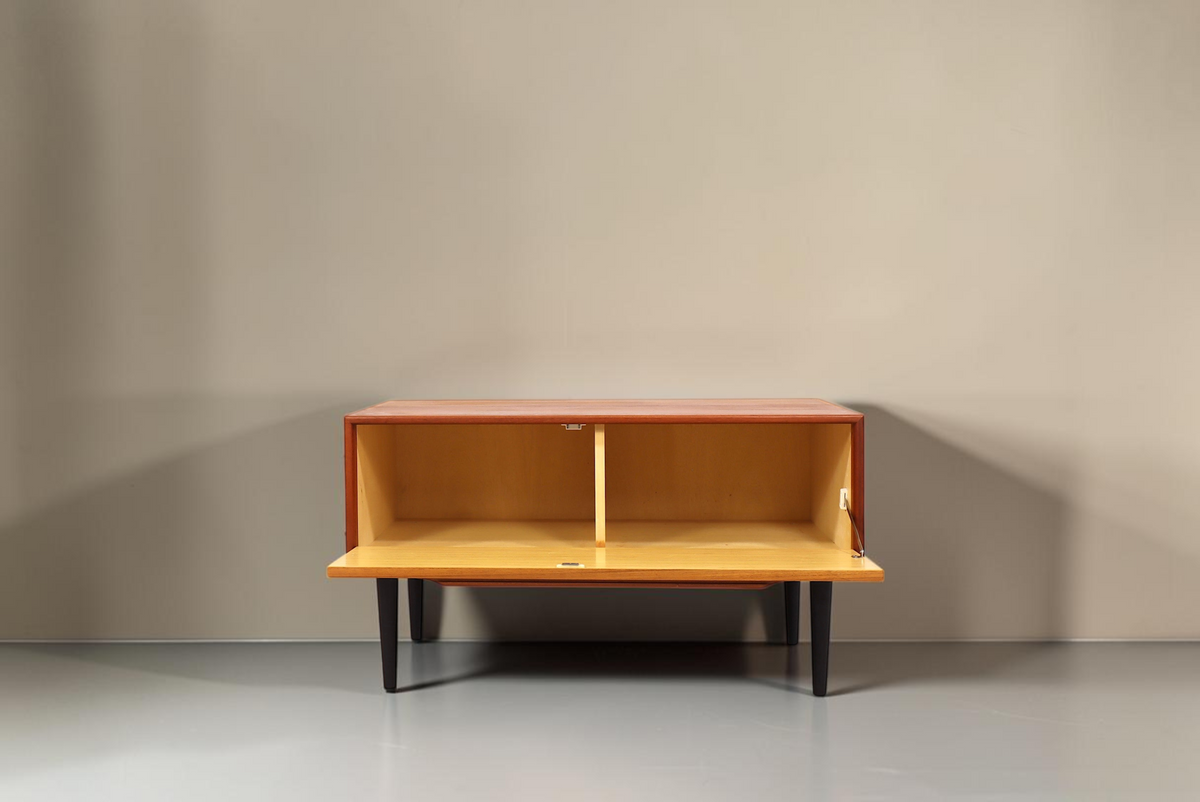 Vintage Space Mid Century Teak Sideboard mit offener Klapptür und schwarzen konischen Füßen vor weißem Hintergrund