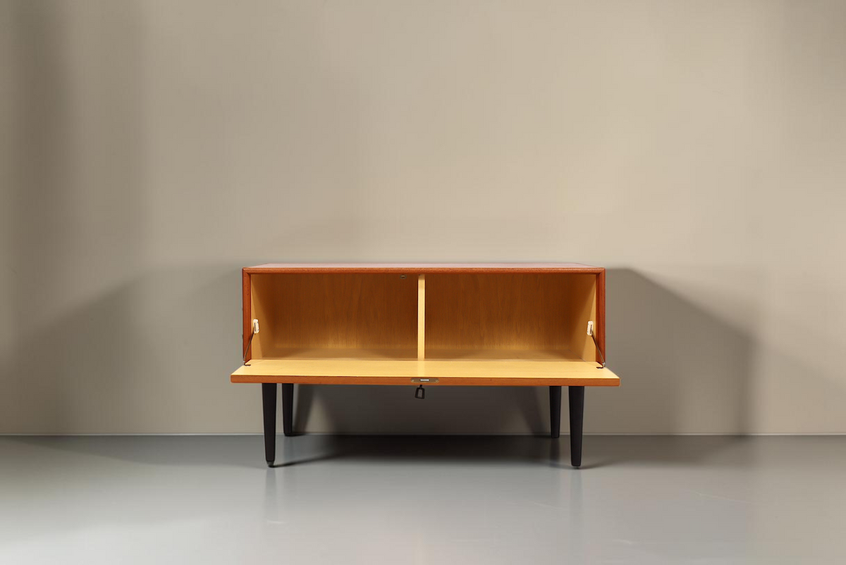 Vintage Space Mid Century Teak Sideboard mit Klapptür und schwarzen konischen Füßen vor weißem Hintergrund